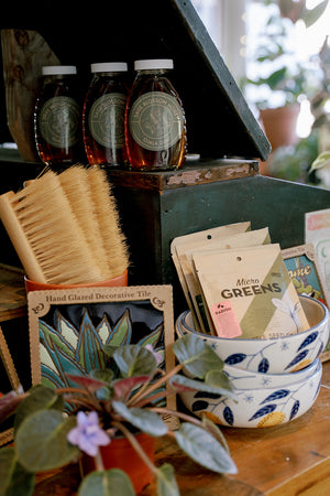 Tabletop display with jars, brushes, decorative tiles, and plant-related products.